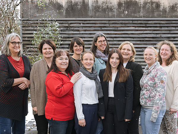 Gruppenfoto von zehn lächelnden Frauen, dem Team der Berufsfachschule Agatharied, die im Freien vor einem Holzgebäude stehen.