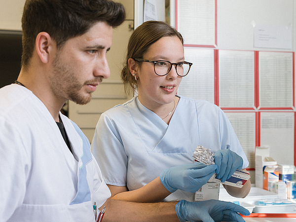 Zwei Auszubildende der Berufsfachschule Agatharied in medizinischer Kleidung und blauen Handschuhen bereiten Medikamente vor.