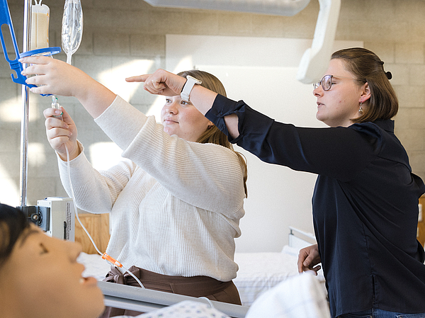 Eine Lehrerin der Berufsfachschule Agatharied zeigt einer Auszubildenden an einer Pflegepuppe, wie eine Infusion vorbereitet und richtig angelegt wird.